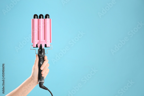 Foto Woman holding triple curling hair iron on light blue background, closeup