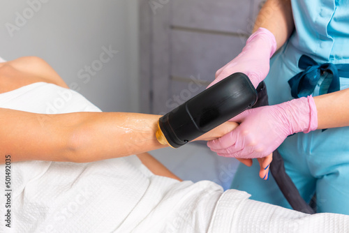 Professional cosmetologist in pink gloves removes hair with laser epilation to the client's female hand. Close up. The concept of professional care procedure in a cosmetology beauty salon