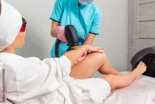 Professional cosmetologist in pink gloves removes hair with laser epilation to the client s female hand. The concept of professional care procedure in a beauty salon