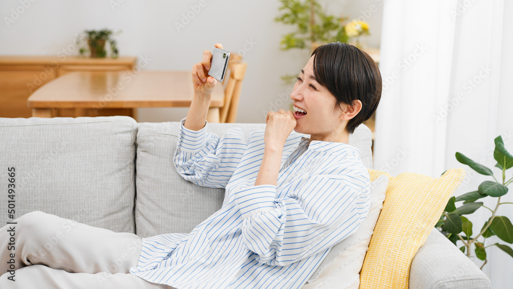 ソファーに座りながらスマートフォンを使う若い女性 ソファーに座りながらスマートフォンを使う若い女性