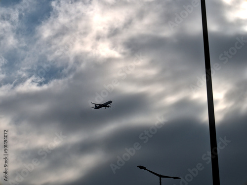 Silhouette of an airplane above the city preparing to land. Dramatic cloudy sky in the background