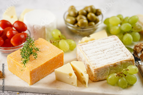 Cheese platter with organic cheeses - blue cheese cheddar, emmantal, french soft cheese with strong smell, italian parmesan, grapes, tomatoes, olives, nuts and crackers on marble board