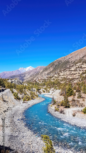 A panoramic view on river in Himalayan valley seen from Annapurna Circuit Trek, Nepal. Turquoise color of the river, big stones popping out of the river. Green forest around. Idyllic landscape. photo