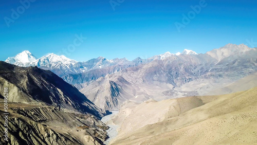 A panoramic view on dry Himalayan landscape. Located in Mustang region, Annapurna Circuit Trek in Nepal. In the back there is snow capped Dhaulagiri I. Barren and steep slopes. Harsh condition.