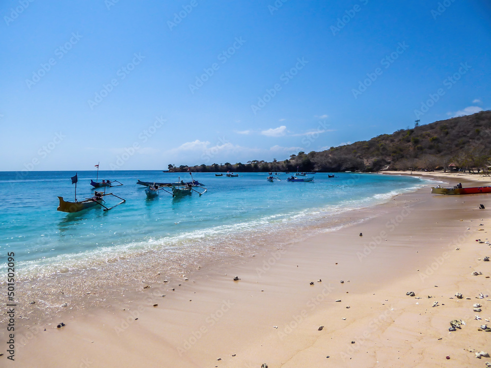 A view on an idyllic Pink Beach on Lombok, Indonesia. Many boats drifting on a calm surface of the sea, some anchored to the shore. Unspoiled, hidden gem. Perfect place for peaceful, relaxed holidays A view on an idyllic Pink Beach on Lombok, Indonesia. Many boats drifting on a calm surface of the sea, some anchored to the shore. Unspoiled, hidden gem. Perfect place for peaceful, relaxed holidays