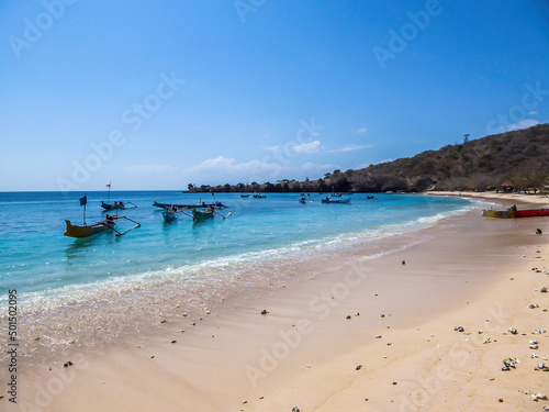 A view on an idyllic Pink Beach on Lombok, Indonesia. Many boats drifting on a calm surface of the sea, some anchored to the shore. Unspoiled, hidden gem. Perfect place for peaceful, relaxed holidays
