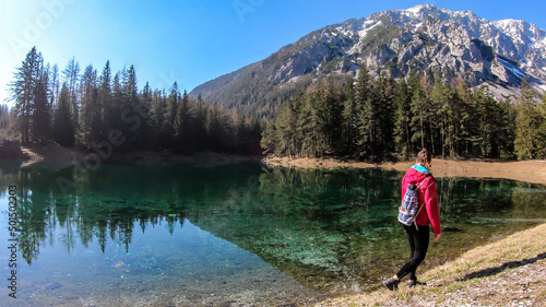 Woman enjoying a peaceful Green Lake, located in an Alpine valley in Austria. The algae in the lake give it its distinctive color. Lots of pine trees on the shore. The girl is walking along the lake.