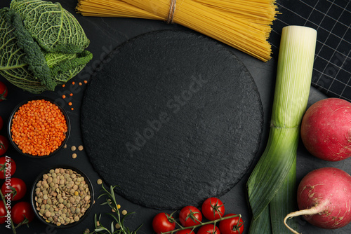 Fototapeta Naklejka Na Ścianę i Meble -  Slate plate surrounded by different ingredients on black table, flat lay with space for text. Cooking classes