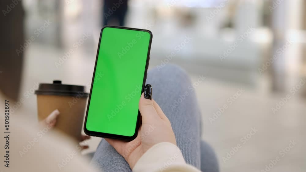 Shopping center. Rear view of a brunette holding a smartphone with a green screen with a chroma key browsing content. Online shopping. Gadgets and modern people concept. Girl sitting in a mall with Shopping center. Rear view of a brunette holding a smartphone with a green screen with a chroma key browsing content. Online shopping. Gadgets and modern people concept. Girl sitting in a mall with