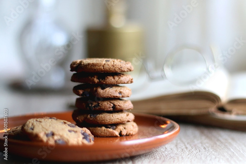 Wallpaper Mural Stack of chocolate chip cookies, open book and reading glasses, lit candle and vase with flowers on the table. Hygge at home. Selective focus. Torontodigital.ca