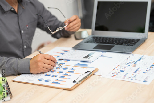close up of businessman hand working on laptop computer with business graph information diagram on wooden desk as concept