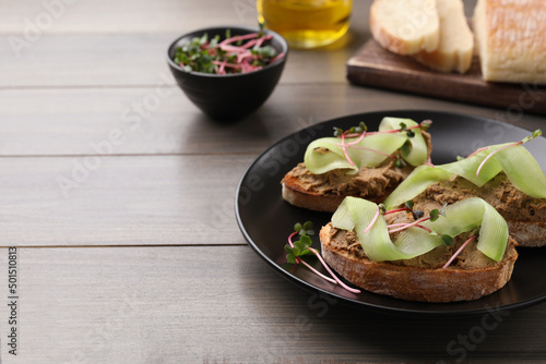 Slices of bread with delicious pate, cucumber and microgreens on wooden table, space for text