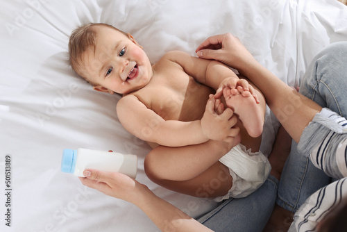 Mother with bottle of dusting powder near her cute baby on bed, top view