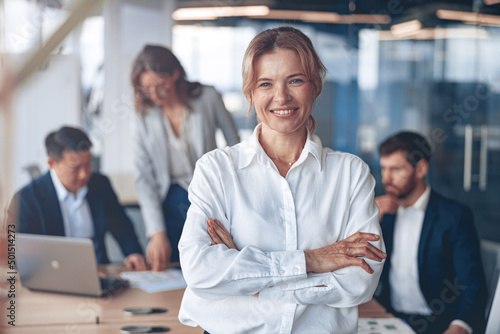 Portrait of beautiful smiling mature businesswoman with her colleagues on background in office.