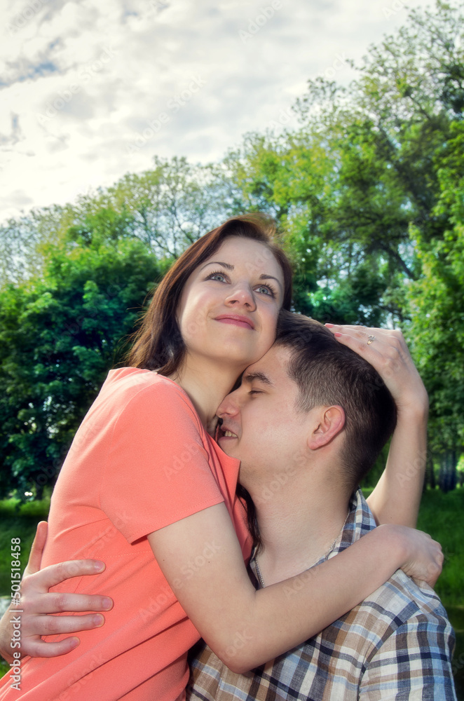 A girl in a pink dress is sitting on the lap of a guy on a park bench. A love story of a beautiful loving couple. A girl in a pink dress is sitting on the lap of a guy on a park bench. A love story of a beautiful loving couple.
