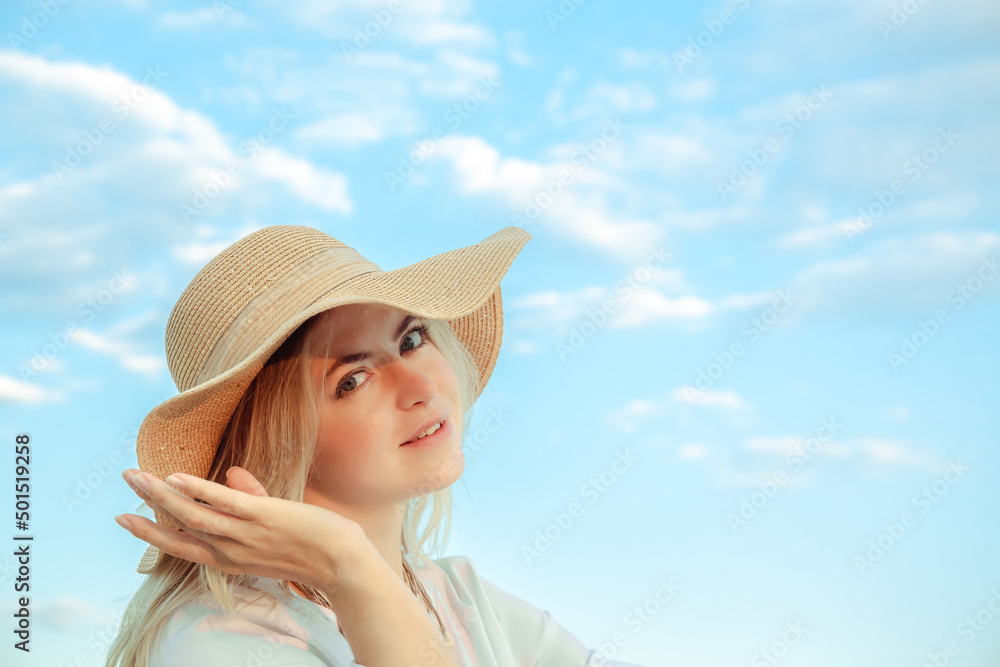 Portrait of young 30 year european woman in straw hat and white dress looking at the camera on a cloudy sky background. Beautiful girl. Side view. Profile. Romance mood. International woman day. Hand