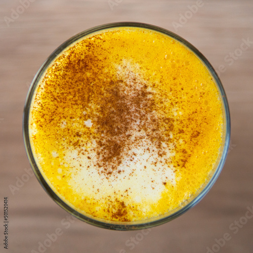 Top view of a yellow barraquito with cinnamon powder on top, over a background of the table photo