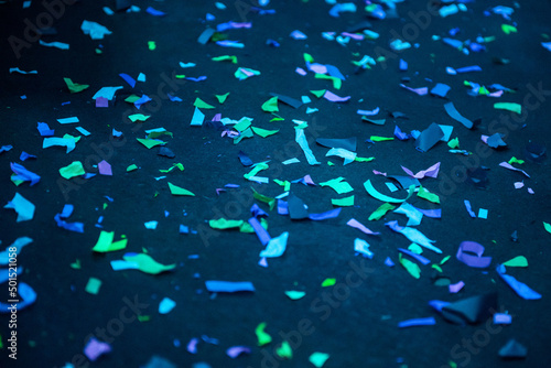 Thousands of confetti on the floor during a night festival. Image is ideal for backgrounds. Multicolor are the confetti in the photo. The floor as a background is black. Cold and blue tonality