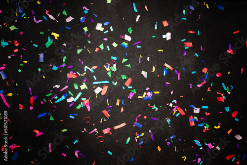 Thousands of confetti on the floor during a night festival. Image is ideal for backgrounds. Multicolor are the confetti in the photo. The floor as a background is black. 