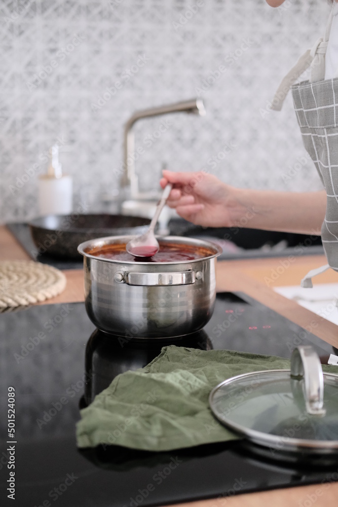 Woman in apron cooking delicious borscht soup on the hob Woman in apron cooking delicious borscht soup on the hob