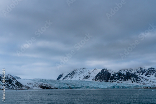 Melting glacier in Svalbard, Norway, with dark winter mountain with snow, sea.
