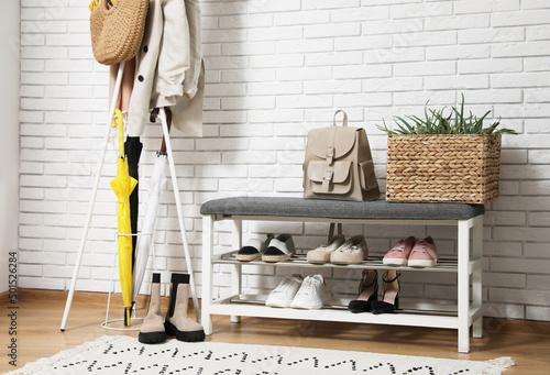 Stylish hallway interior with coat rack and shoe storage bench near white brick wall