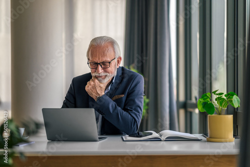 Fotobehang Serious elderly entrepreneur working on laptop while sitting at office desk