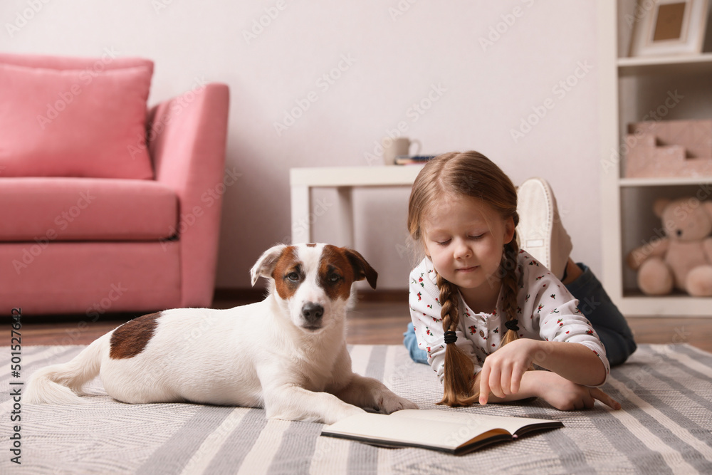 Cute little girl with her dog reading book on carpet at home. Childhood pet Cute little girl with her dog reading book on carpet at home. Childhood pet