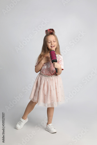 Cute little girl with hairbrush singing on light grey background © New Africa