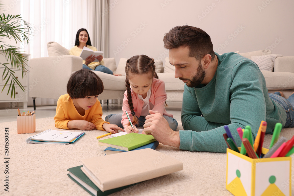Father playing with his children while mother reading book on sofa in living room