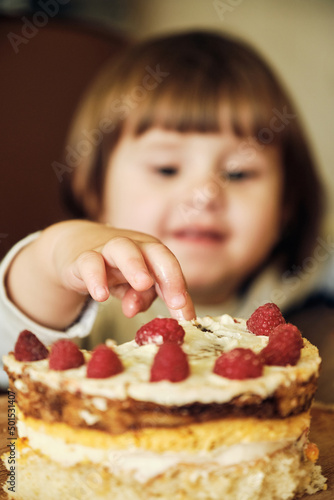 Cute Happy Baby Girl Eating Cake With Raspberries. Adorable little girl Tasting Cream On Cake.