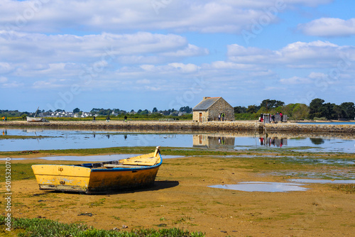 Vue lointaine d'une barque jaune et bleue posée sur le sable à la marée basse sur l'île d'Arz dans le golfe du Morbihan photo