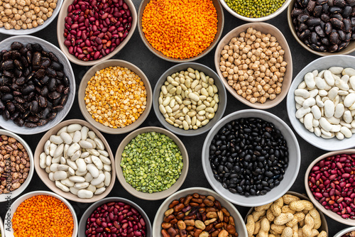 Different types of legumes in bowls, green with yellow peas and mung beans, chickpeas and peanuts, colored beans and lentils, top view