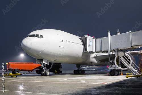 Close-up white wide body passenger airliner stands at the jet bridge on night airport apron