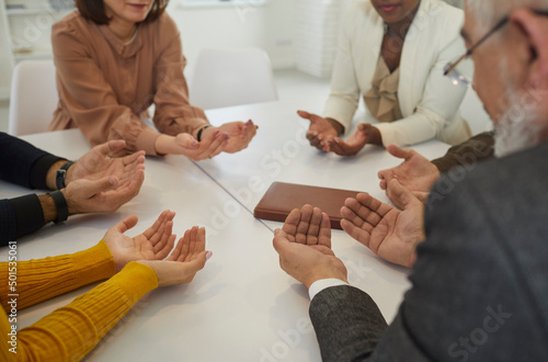 People who believe in God praying together. Group of different young and senior multiracial Christians sitting around the table with their palms facing up and saying a prayer to God. Faith concept