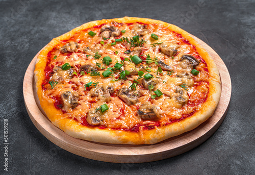 Pizza with mushrooms, cheese, tomatoes and herbs on a cutting board on a dark background. Fast food. Side view, close-up.