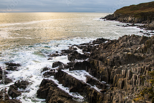 The setting sun casts a golden glow on the sea, which gently laps the dramatic rocks of the North Devon Coast.