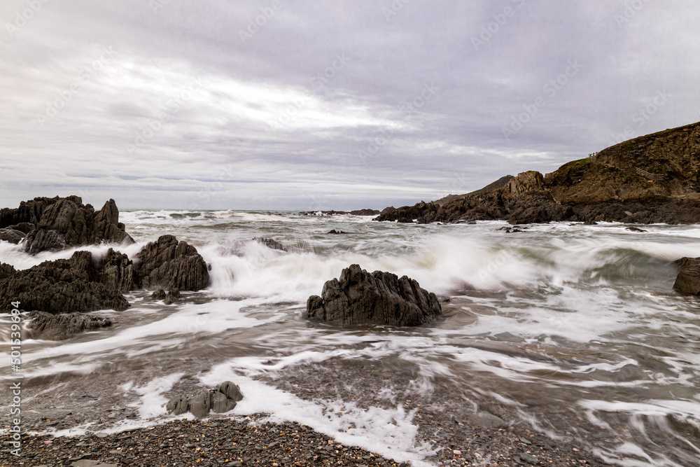 Obraz premium Dark rocks on this Devon Beach, being washed by the waves, as they have been every day for millennia.