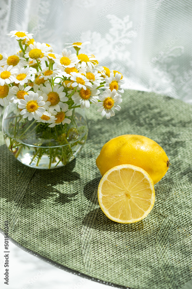 Daisy flowers, whole lemons, on green placemat. Summer still life scene Daisy flowers, whole lemons, on green placemat. Summer still life scene
