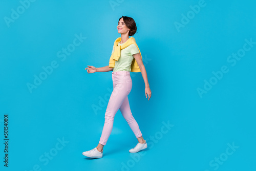 Full size photo of pretty young brunette lady go wear t-shirt pants shoes isolated on blue background