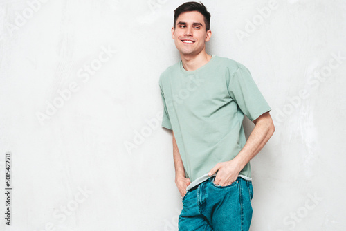 Portrait of handsome smiling stylish hipster lambersexual model.Man dressed in T-shirt and jeans. Fashion male isolated in studio. Posing near grey wall. Cheerful and happy