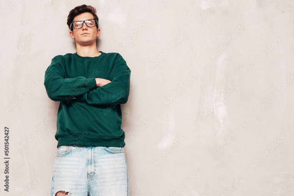 Portrait of handsome confident stylish hipster lambersexual model.Man dressed in green sweater and jeans. Fashion male posing in studio near grey wall Portrait of handsome confident stylish hipster lambersexual model.Man dressed in green sweater and jeans. Fashion male posing in studio near grey wall