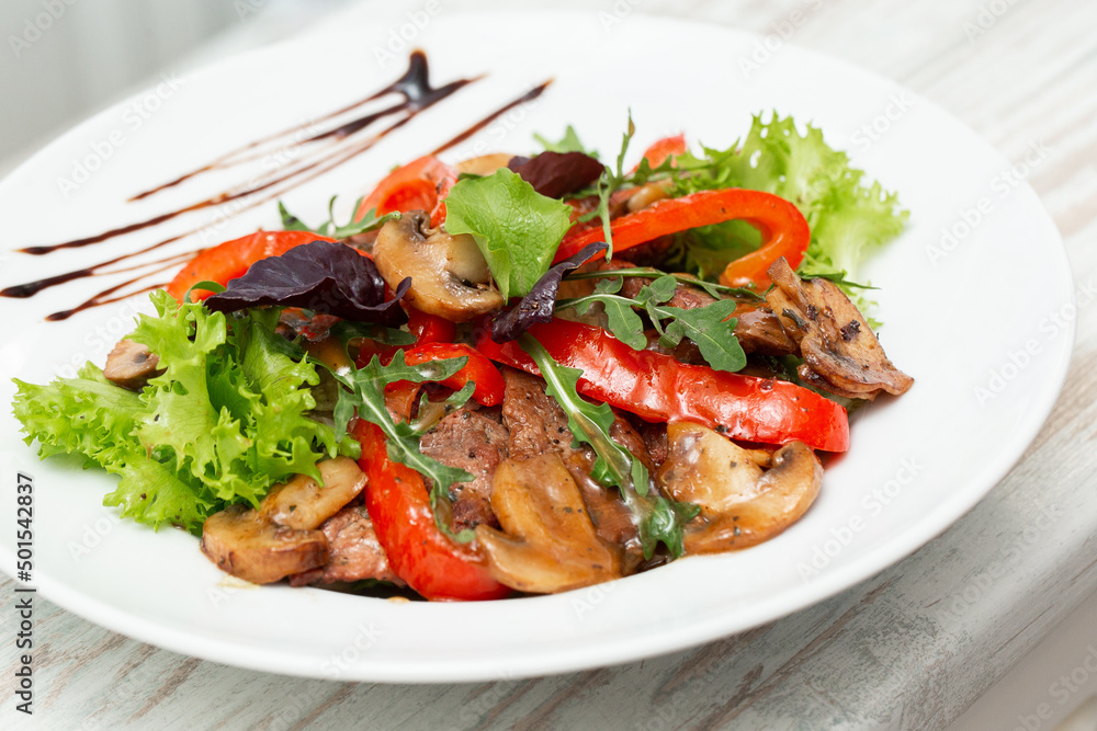 Veal salad with lettuce, red pepper and mushroom on white plate on wooden background, copy space. Restaurant food, close up. Meat salad Veal salad with lettuce, red pepper and mushroom on white plate on wooden background, copy space. Restaurant food, close up. Meat salad