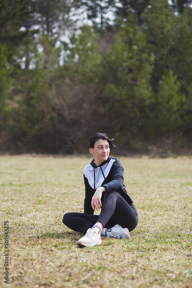 
Young beautiful woman doing exercises outside in front of the forest. Wellness, wellbeing, healthy lifestyle. Fresh air, cottagecore aesthetic. Active, athletic girl working out in spring day