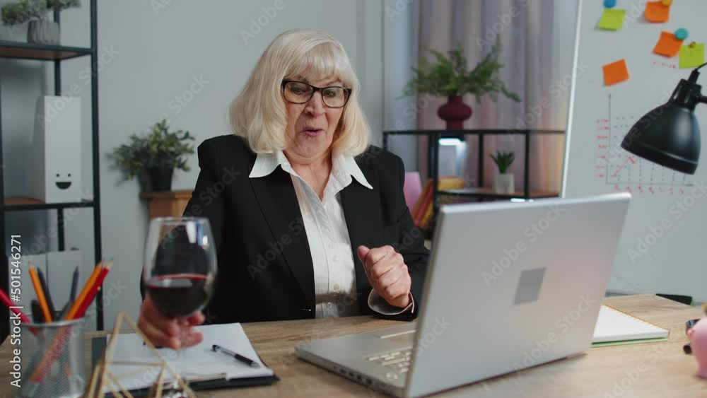Senior business woman freelancer gets good news, positive exam results, opportunity, successfully signed contract, celebrates victory drinking wine after working on laptop computer sitting at office Senior business woman freelancer gets good news, positive exam results, opportunity, successfully signed contract, celebrates victory drinking wine after working on laptop computer sitting at office