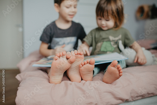 Big brother and little sister holding bare feet close up to camera . Blurred face on background
