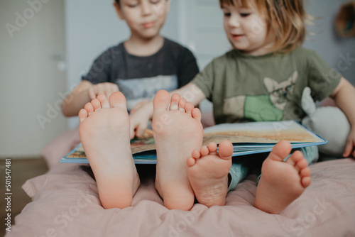 Big brother and little sister holding bare feet close up to camera . Blurred face on background