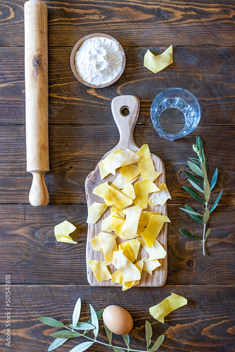 Homemade pasta Maltagliati on cutting board with ingredients on wooden background. Top view photo