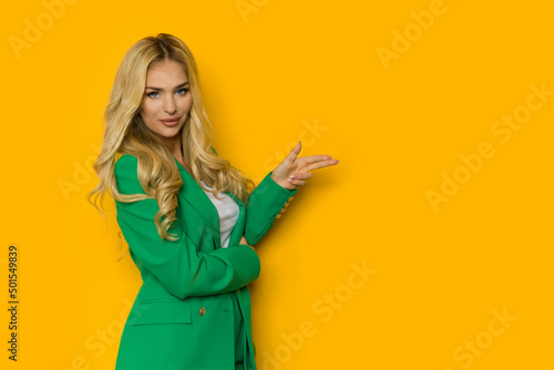 Blond woman in green jacket is pointing with two fingers.
