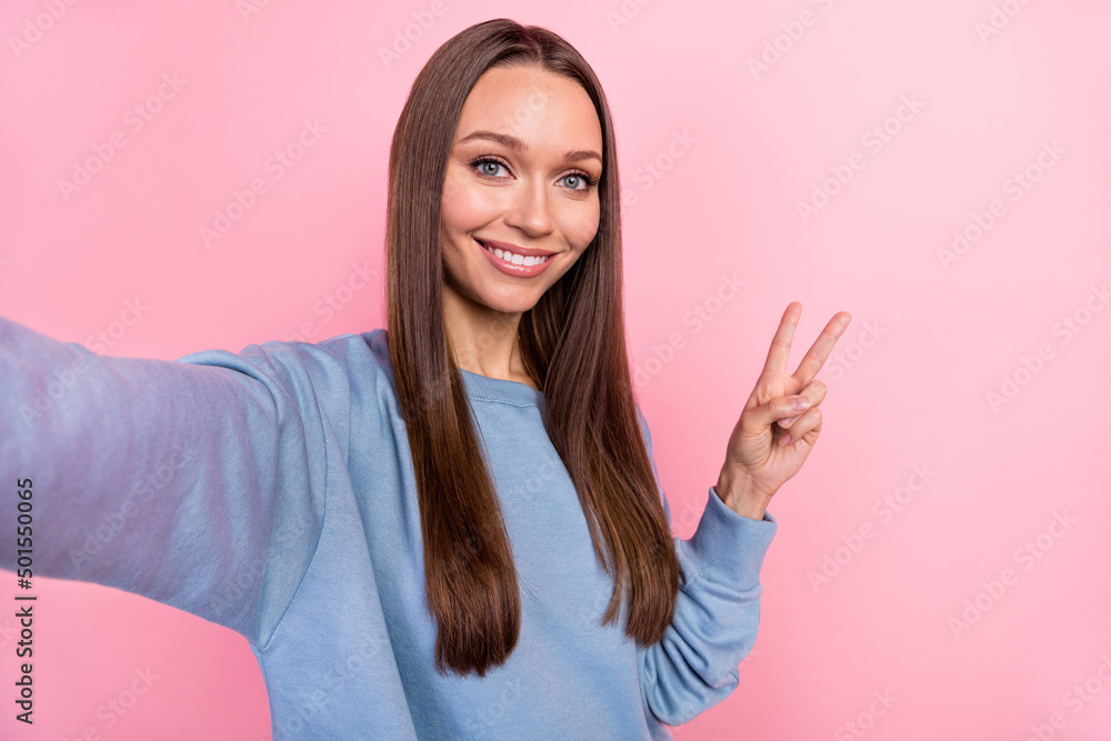 Self-portrait of attractive girly cheerful girl showing v-sign rest isolated over pink pastel color background Self-portrait of attractive girly cheerful girl showing v-sign rest isolated over pink pastel color background